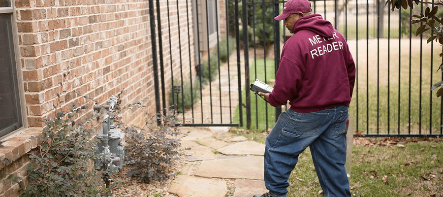 Utility worker checking a residential gas meter near a home with handheld device.