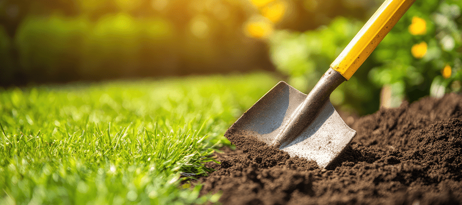 Close-up of a shovel digging into soil beside a grassy lawn, representing safe digging practices before starting outdoor projects.