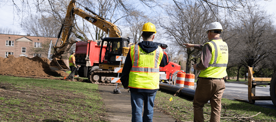 Utility workers oversee excavation activity at a construction site to help prevent underground utility damage and ensure safe digging practices.