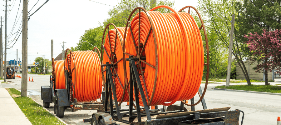 Large reels of orange conduit staged for a broadband project highlight the importance of fiber installation damage prevention and safe excavation practices.